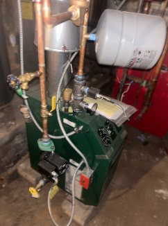 A mechanical device with pipes, valves, gauges, and a tank, possibly part of a heating or plumbing system.