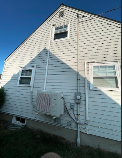 Side of a white house with vinyl siding, featuring two small windows, an air conditioning unit, and electrical meters.