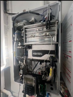 Close-up of a Navien tankless water heater with various pipes and components inside a utility closet.