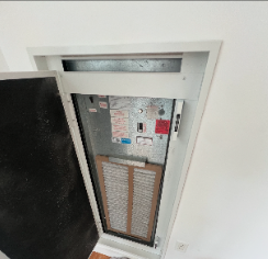View of an indoor vent or air conditioning unit cover with a filter inside, mounted on a white wall near the floor.