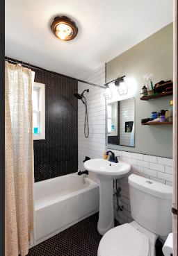 Small bathroom with a bathtub, showerhead, white sink, toilet, mirror, and shelves with toiletries above the toilet.