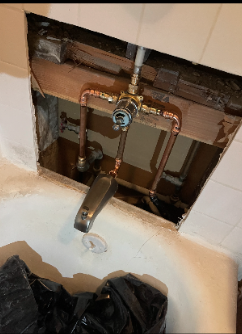 View of a plumbing work area showing exposed copper pipes, a valve, and a faucet above a white sink with some black plastic in the foreground.