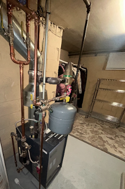 A utility room with pipes, a utility heater, and a water filtering system installed on the wall.