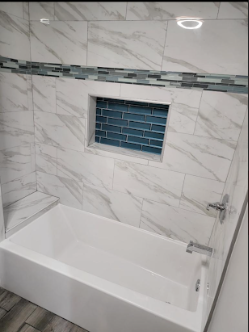 Bathroom with a white bathtub, marble wall tiles, and a recessed wall niche with blue tiles.