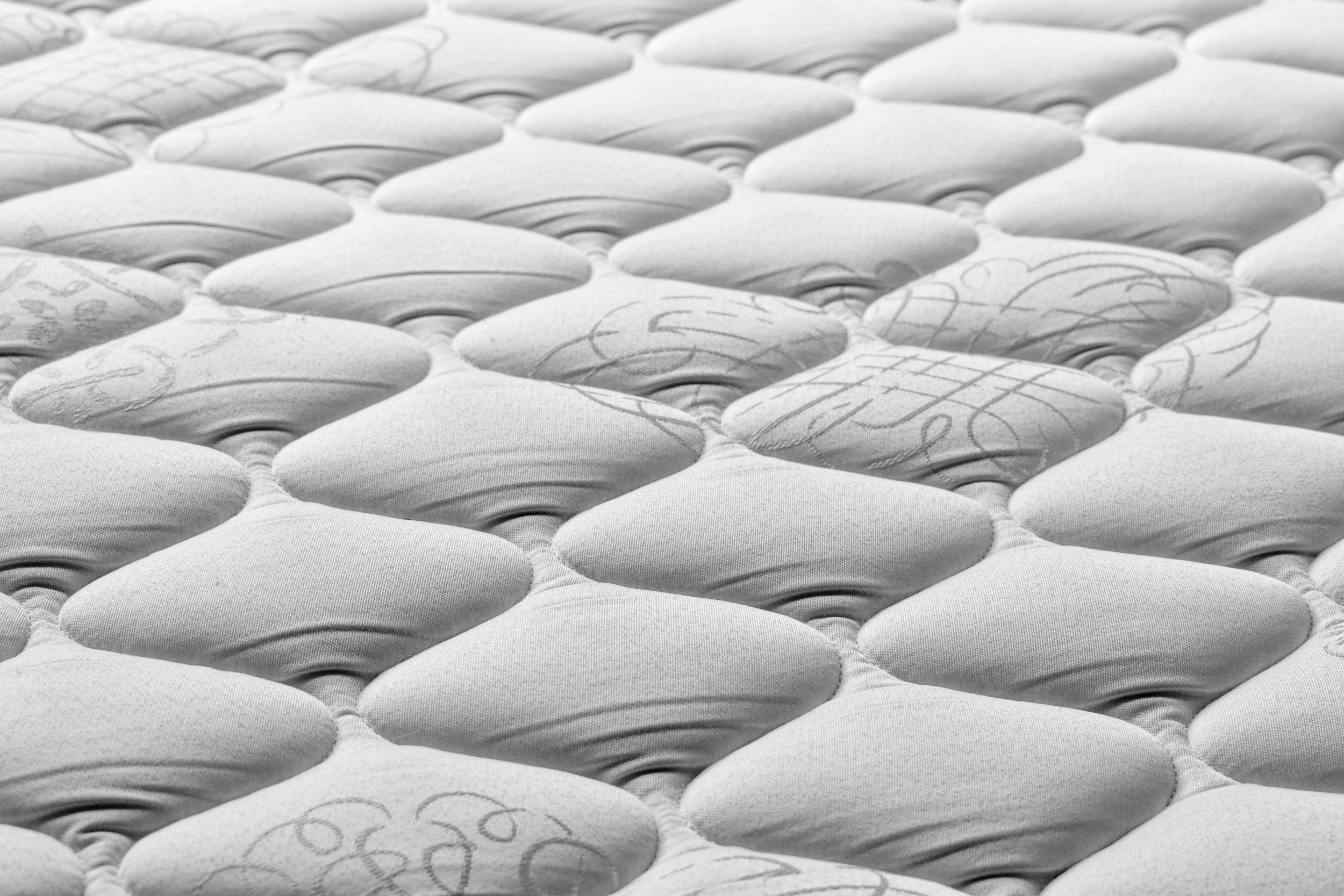Close-up of a mattress with a tufted, diamond pattern and some embroidered details.