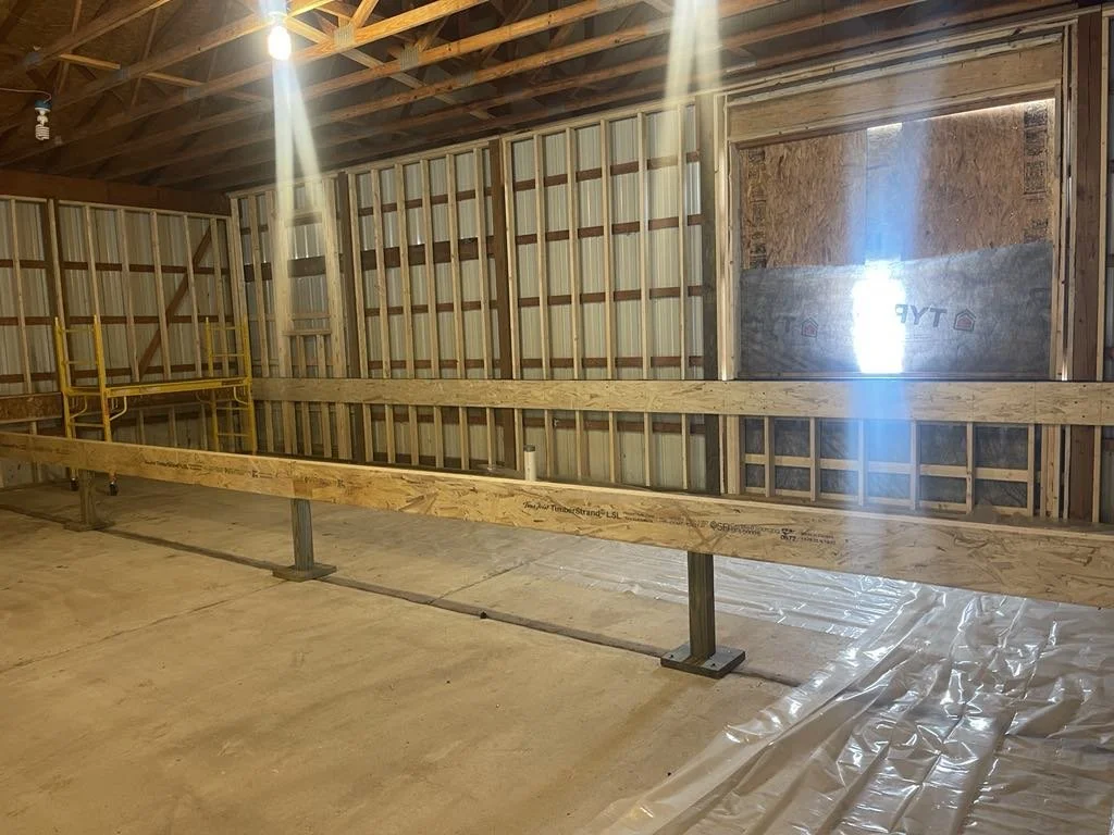 Interior of a building under construction with wooden framing, metal support beams, a small window, and scaffolding on the left side.