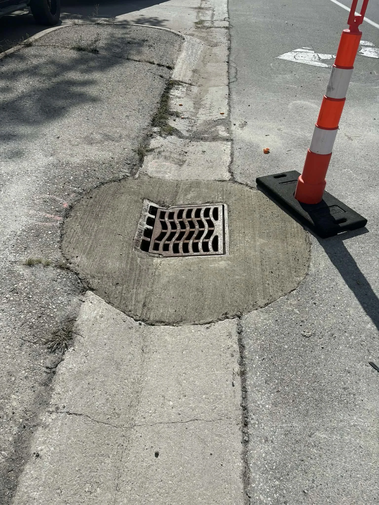 Street sidewalk with a finished storm drain and a traffic cone.
