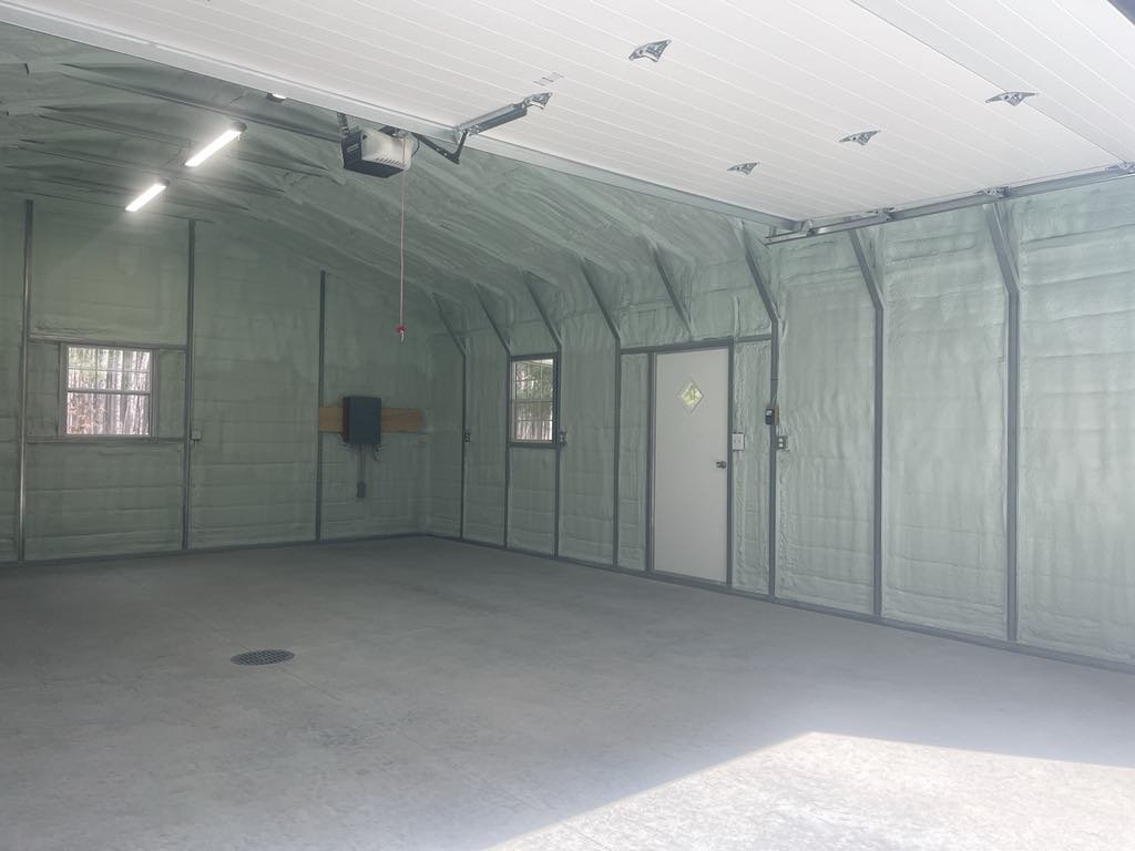Empty garage with spray foam insulation on the walls, a concrete floor, overhead door, and garage door opener system.