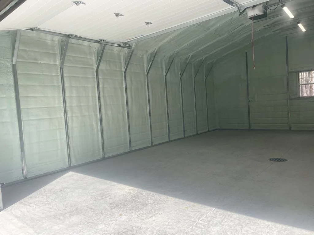 Empty garage with metal framing, spray foam insulation, a concrete floor, and a small window on the right wall.