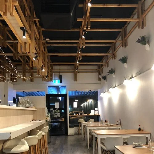 Interior of a modern restaurant with wooden ceiling decor, white walls, and hanging greenery.