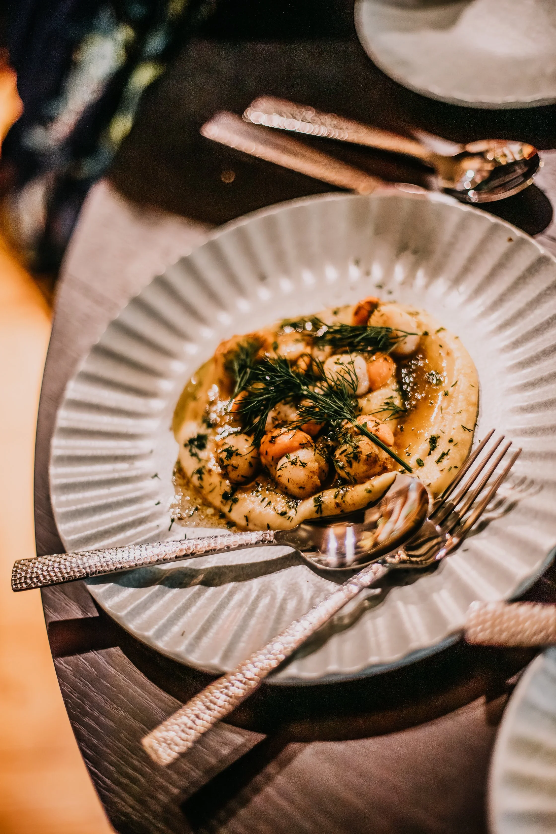 A plated dish of gnocchi with herbs, garnished with fresh dill, on a textured ceramic plate, with silverware nearby.