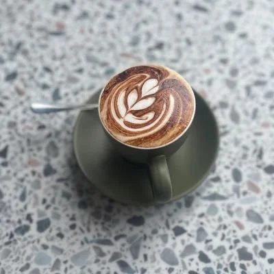 A cup of coffee with latte art on top, placed on a saucer on a speckled countertop.