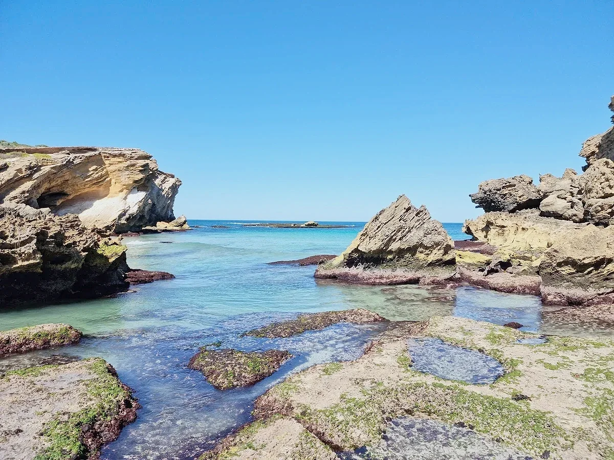 A rocky shoreline with clear blue water under a bright blue sky.
