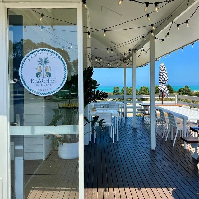 Ocean view from a patio of Beaches Café & Bar with outdoor seating, string lights, and umbrellas.