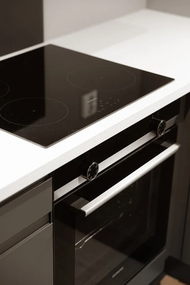 A black electric stove with a digital control panel, located above a black oven, installed in a white kitchen countertop.