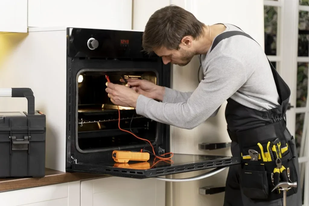 A man repairing an oven with a multimeter and tools.