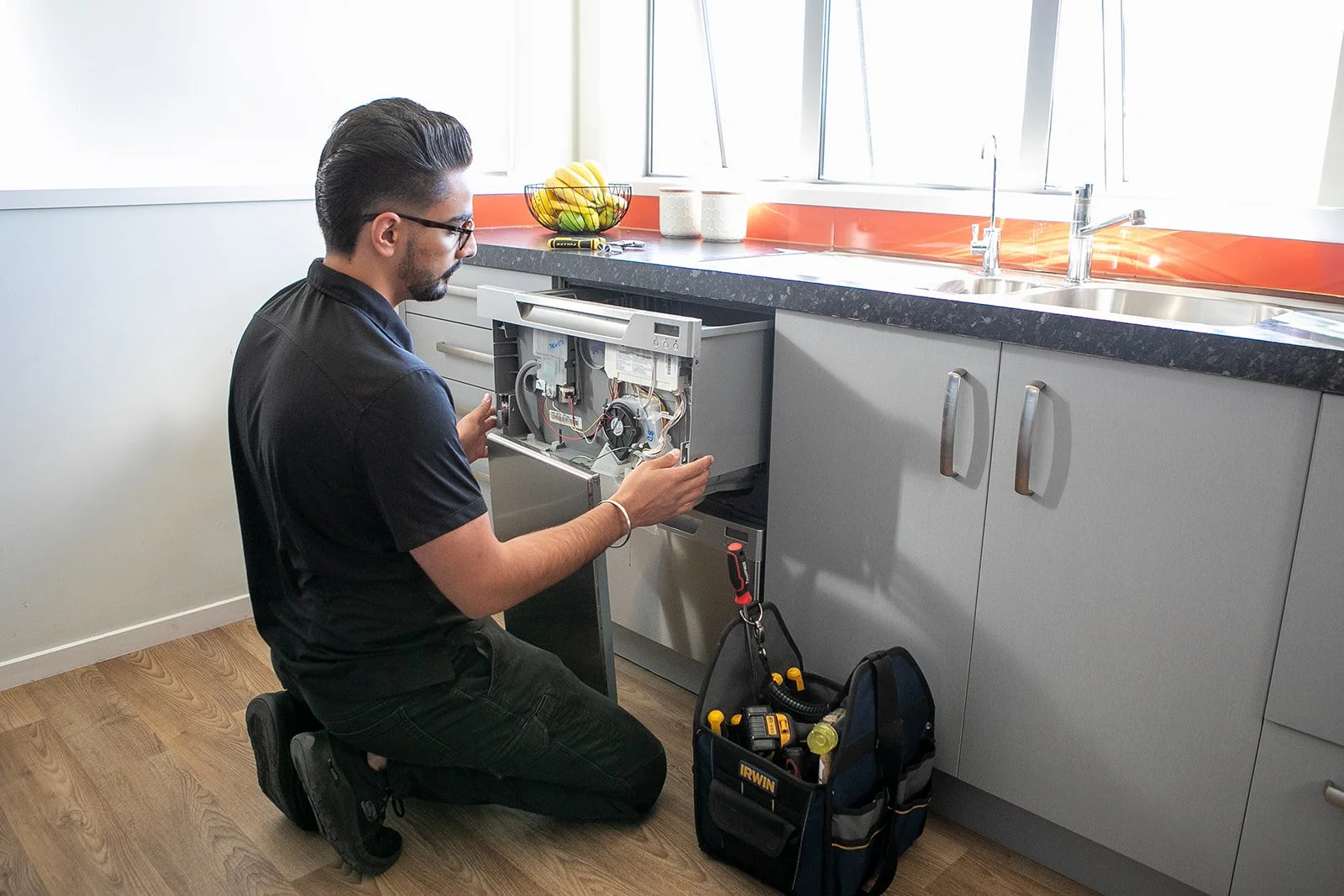 A technician repairing a dishwasher in a modern kitchen.