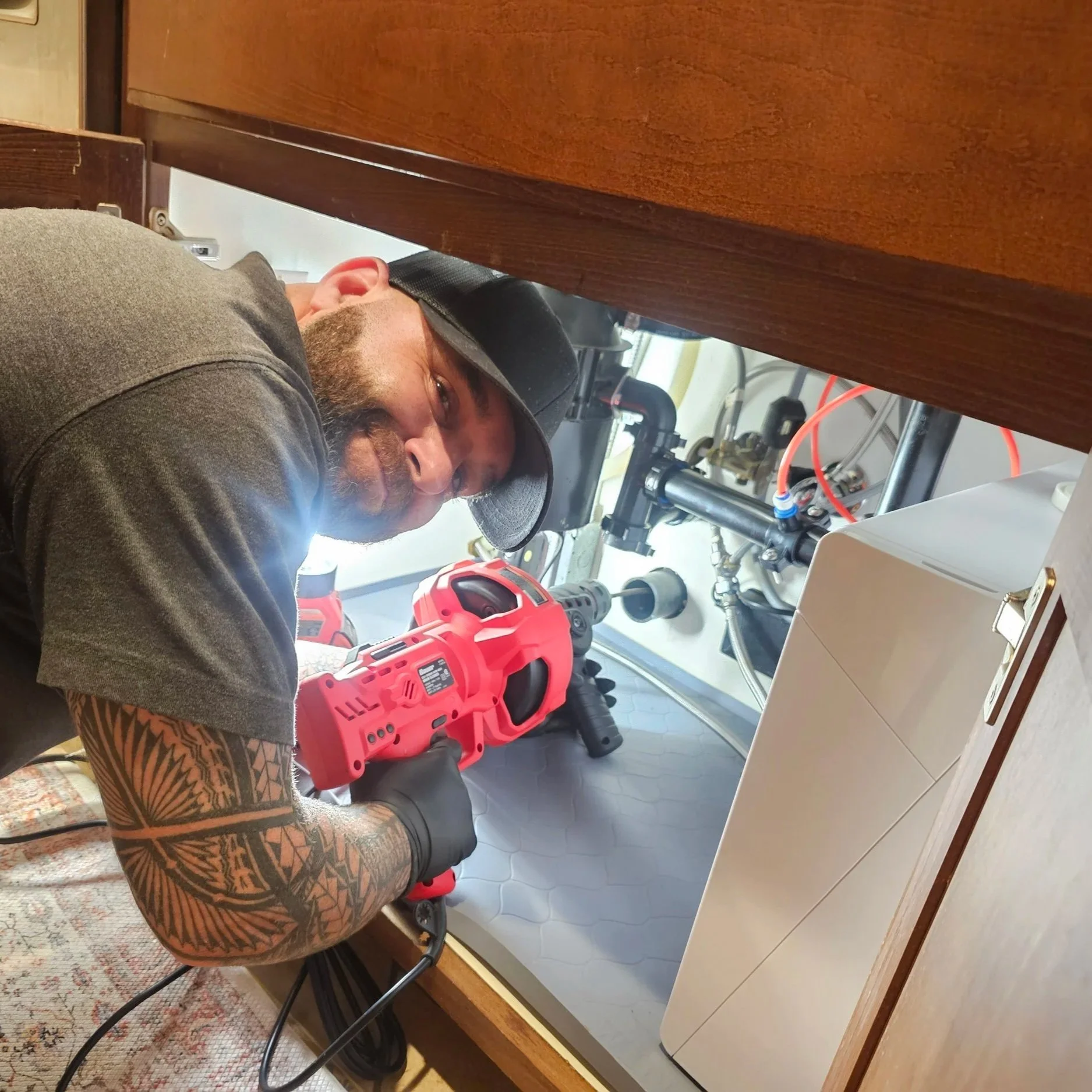 Daniel Davis of Emerald Systems removing a clogged garbage disposal under a kitchen sink, providing reliable plumbing and repair services in the East Bay area.