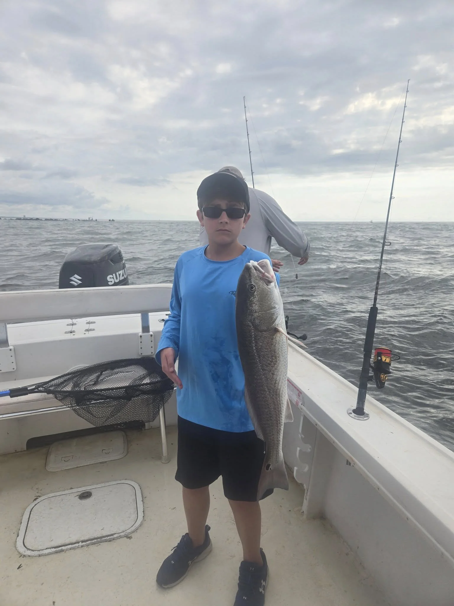 Boy wearing sunglasses in blue shirt holding a large fish on a boat in the ocean under a cloudy sky. Fishing Myrtle Beach near Little River SC fishing charters dolphin cruises boat tours in Little River SC