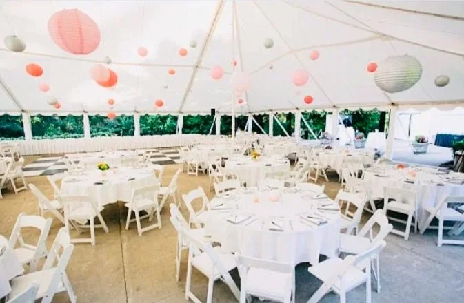 Event tent decorated for a celebration with round tables, white chairs, and pastel paper lanterns hanging from the ceiling.