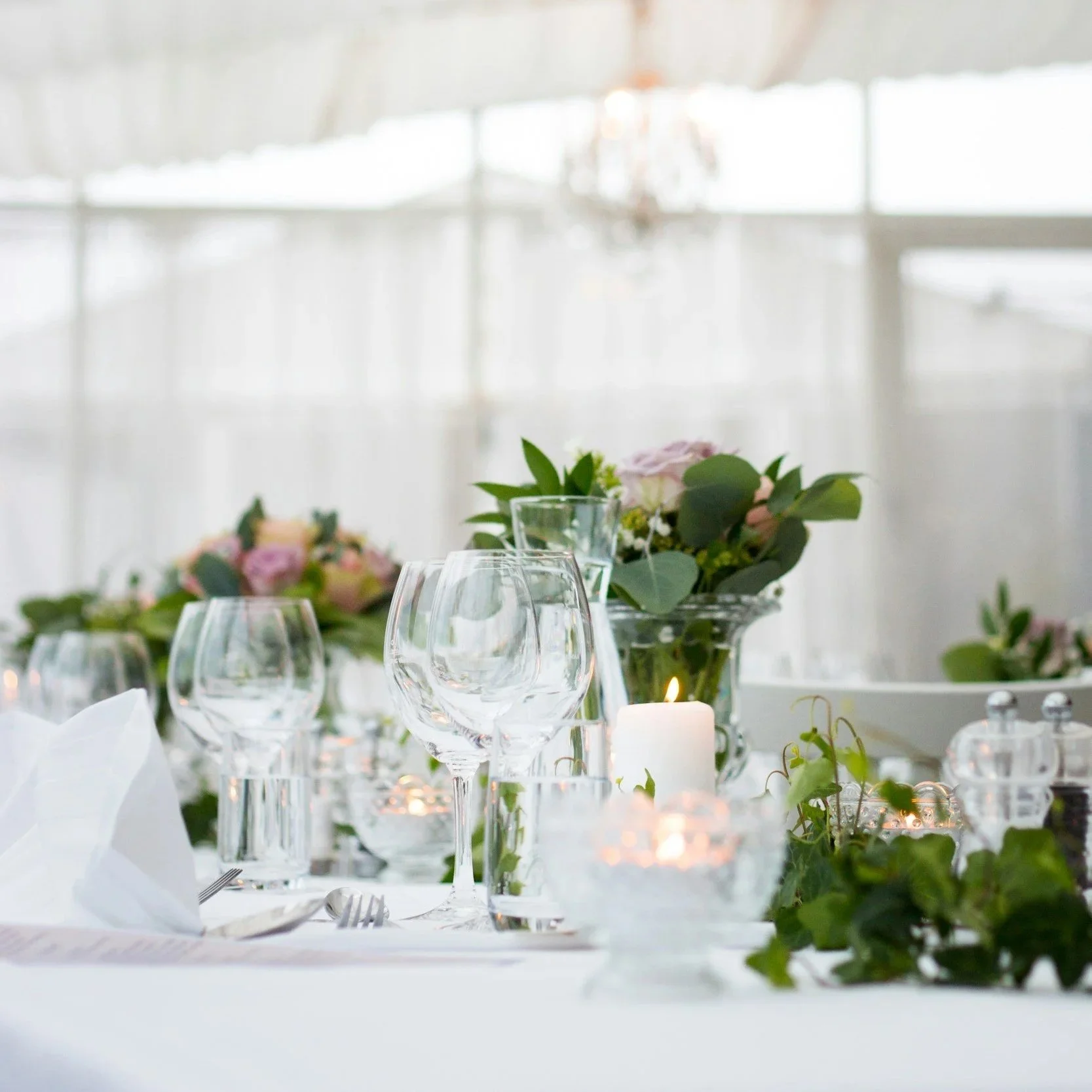 Elegant table setting with wine glasses, floral arrangements, candles, and greenery, set for a formal event or celebration.
