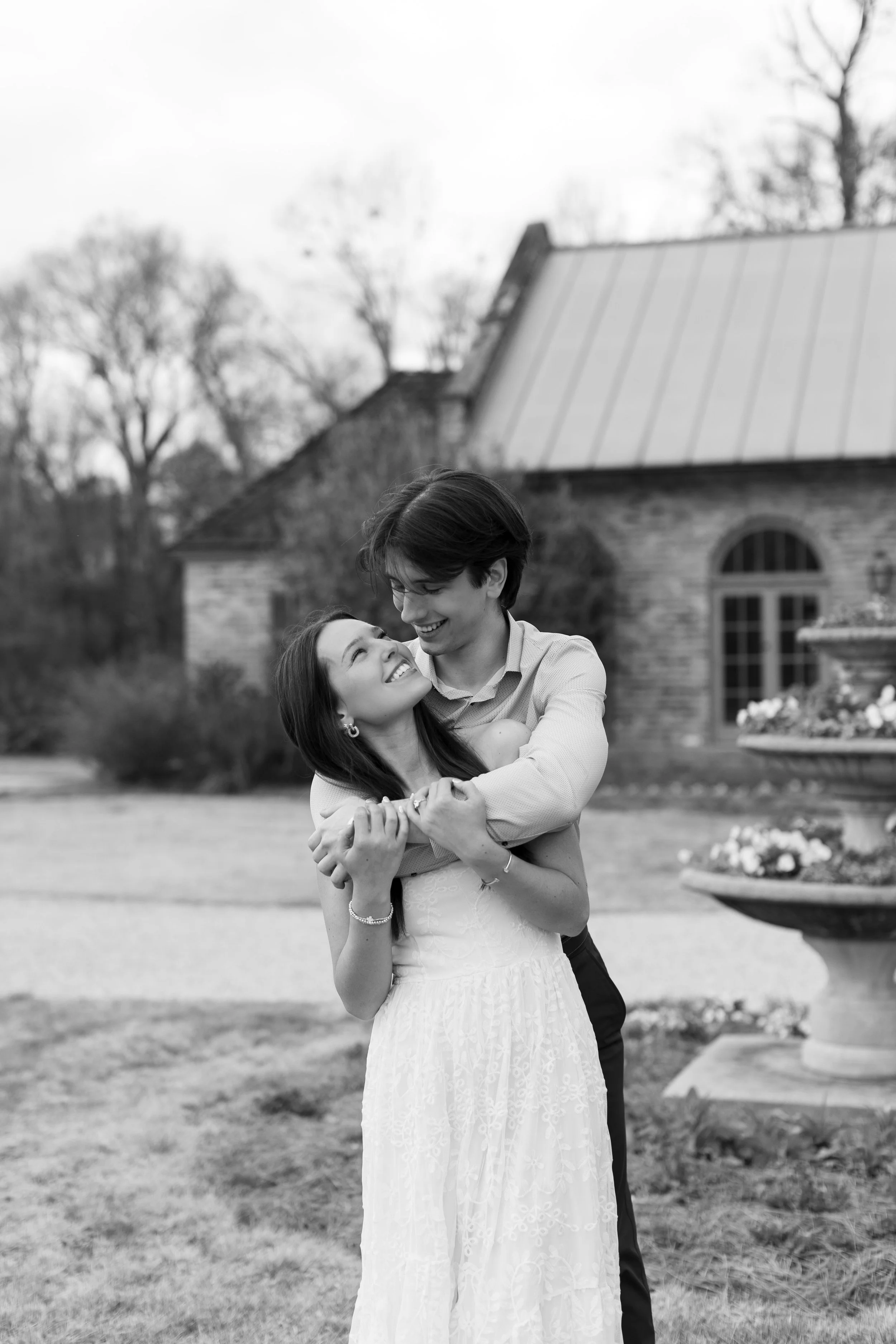 A happy couple hugging outdoors in front of a house, smiling at each other, black and white photo.