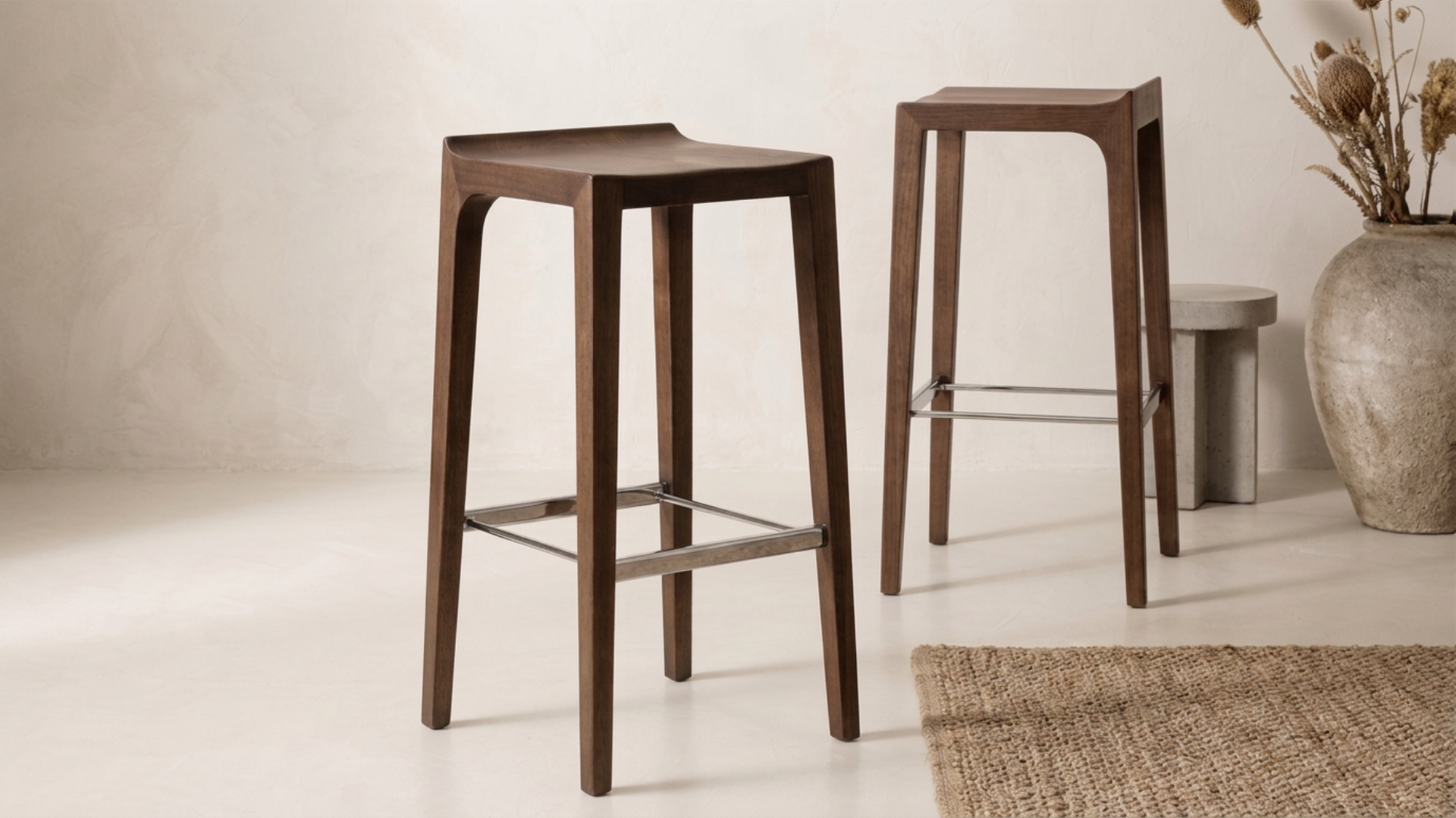 Two modern dark wood bar stools with metal footrests in a minimalist room
