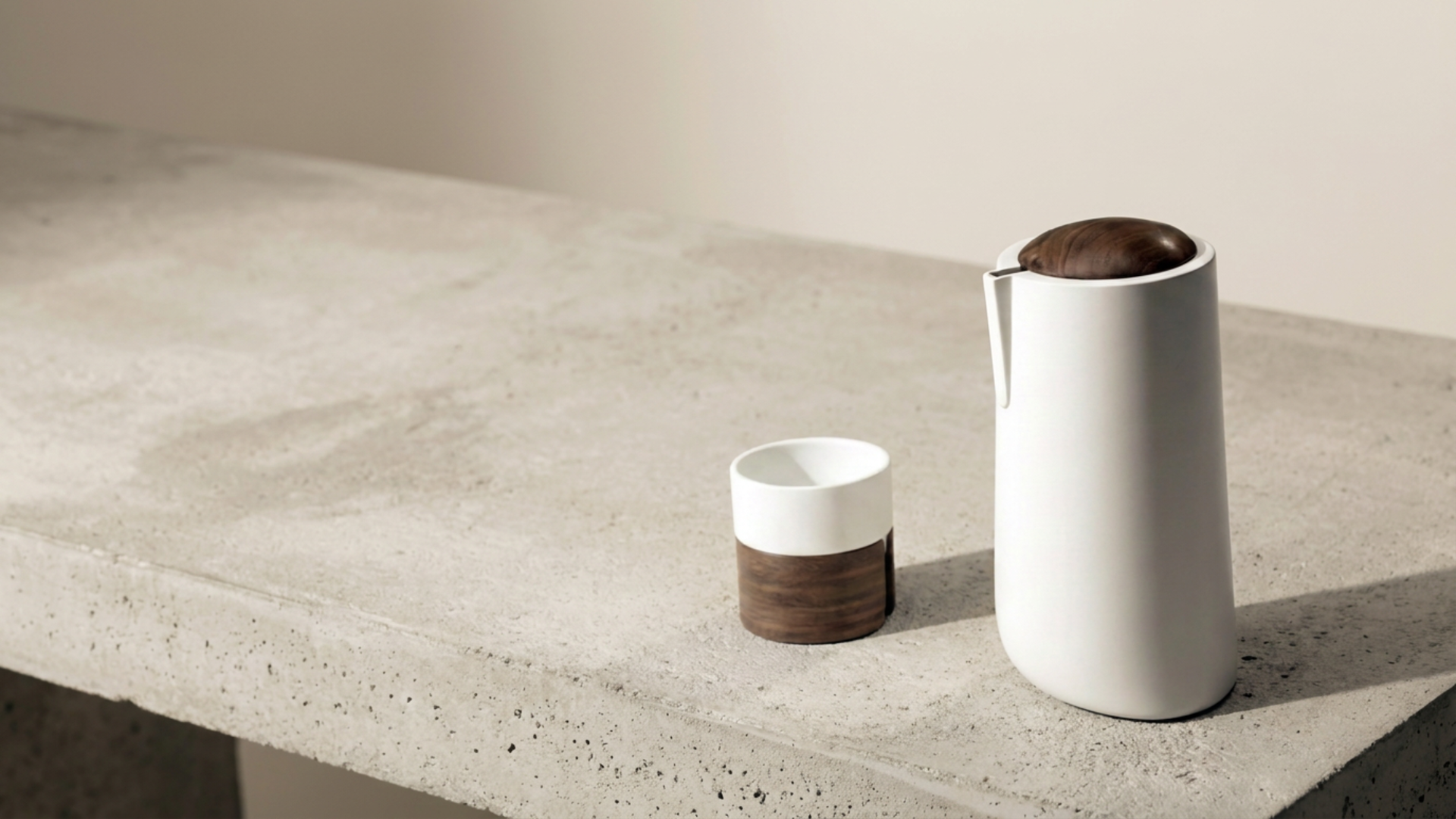 A minimalist white and wood coffee carafe with a matching cup on a concrete countertop.