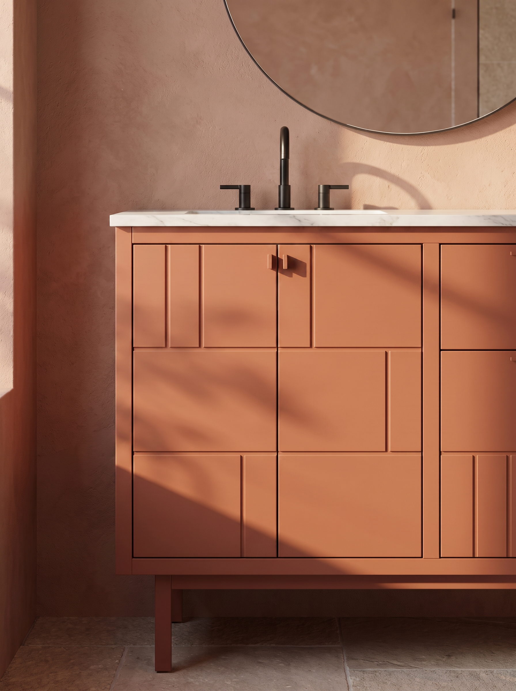 A bathroom vanity with a white marble countertop, black faucet, and matching black handles on a pinkish-brown wooden cabinet, with a large oval mirror above and soft natural lighting.