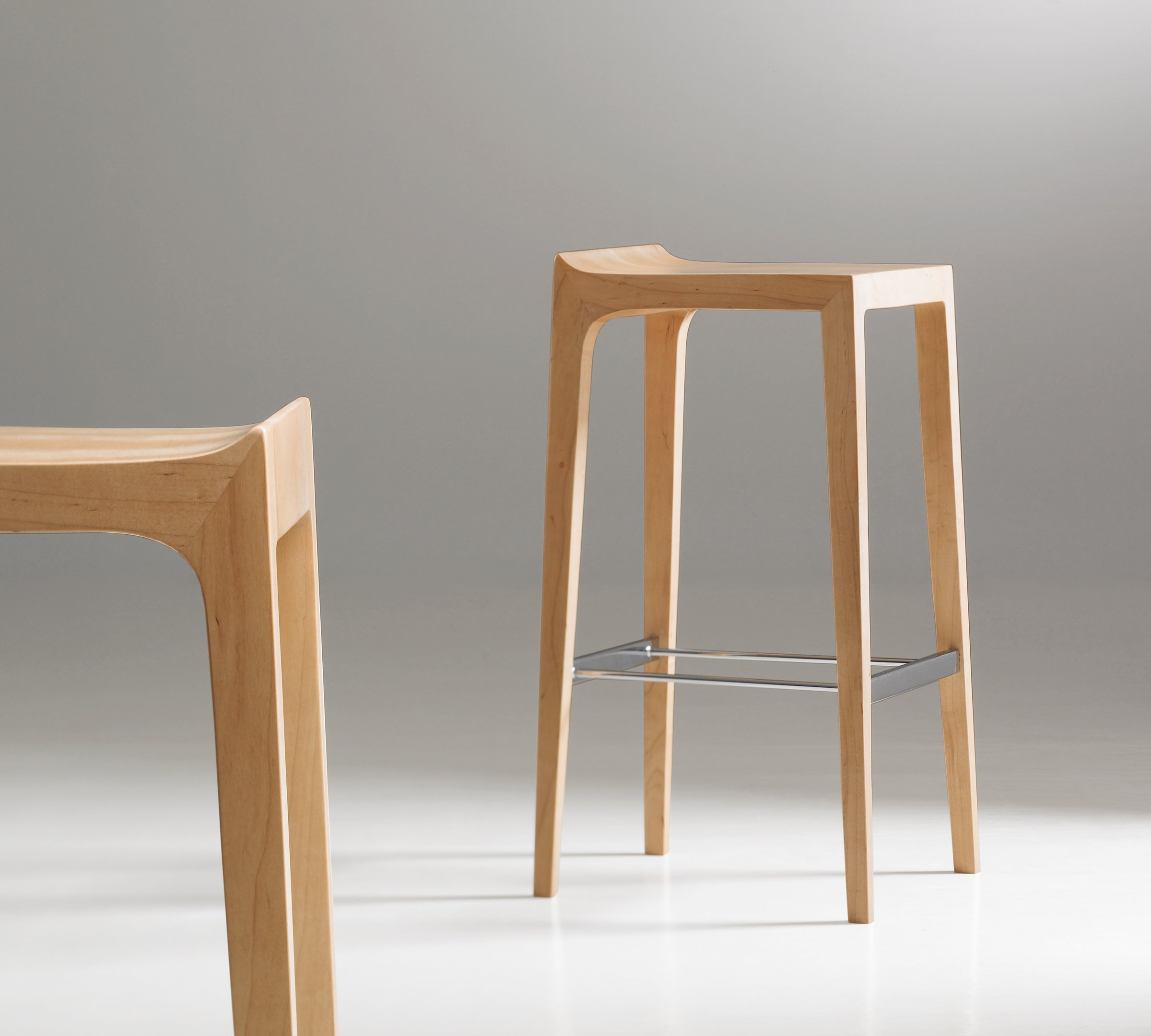 Modern light wood bar stools with curved seats and metal footrests against a gray background