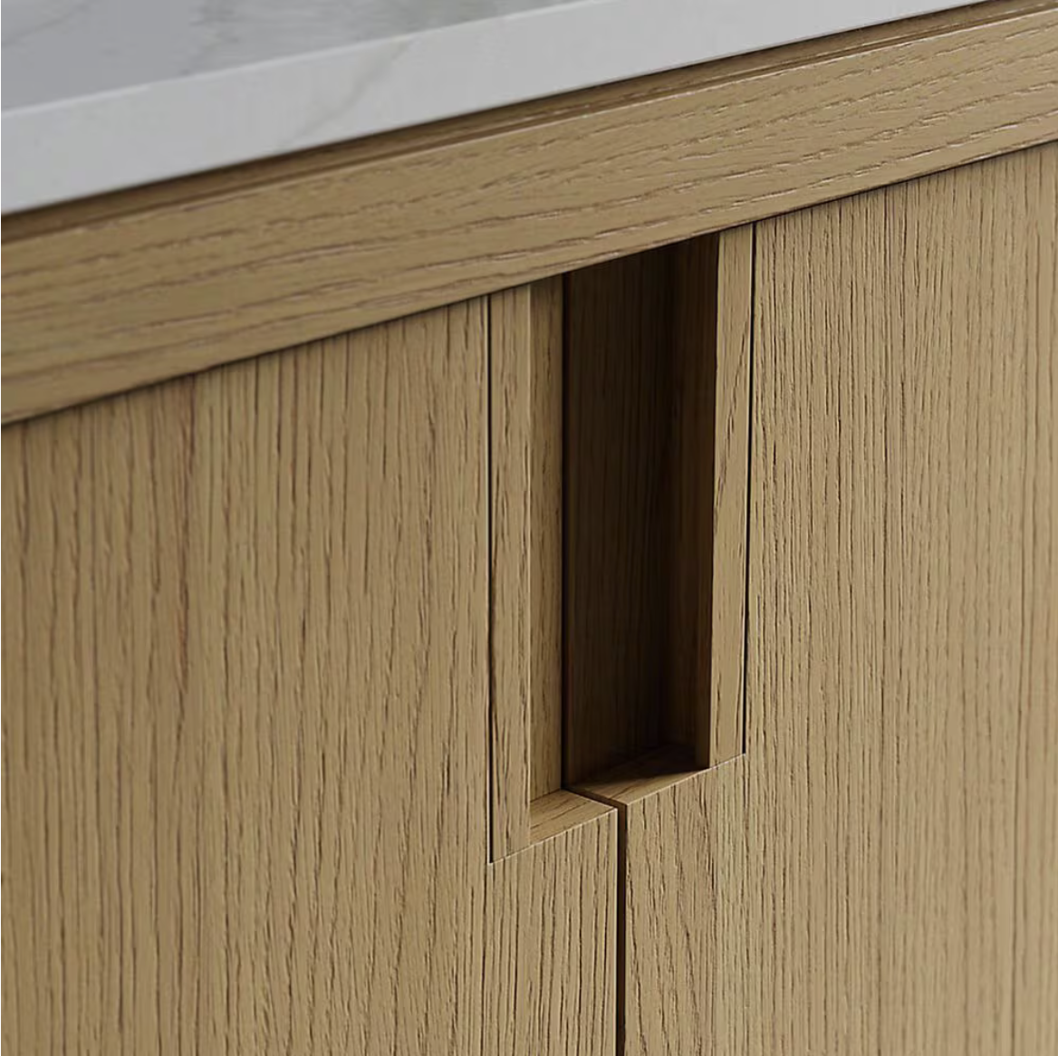 Close-up of a modern oak wood cabinet door with a recessed vertical handle and white countertop