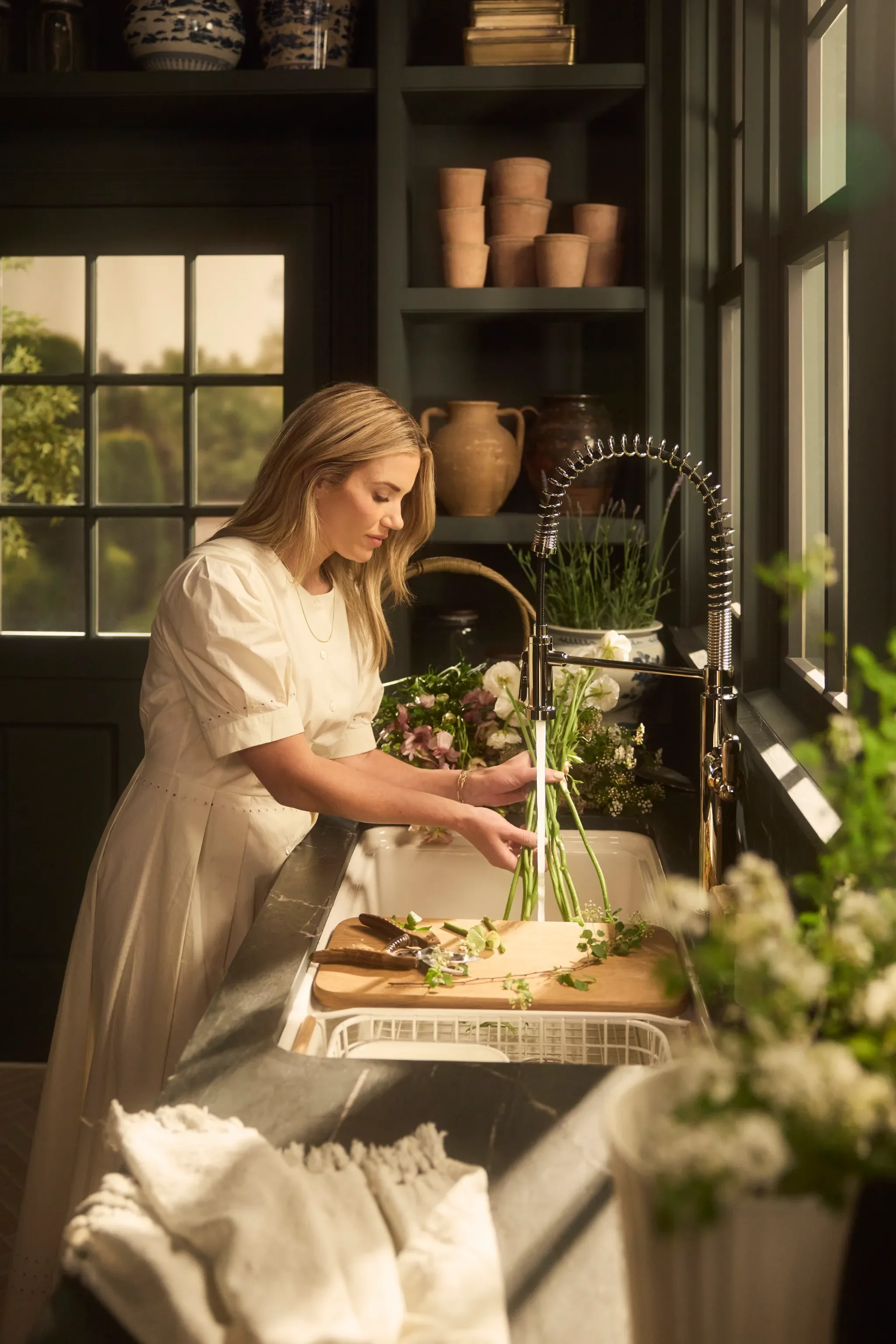 Woman rinsing freshly cut flowers at a kitchen sink beneath a spring-coil faucet