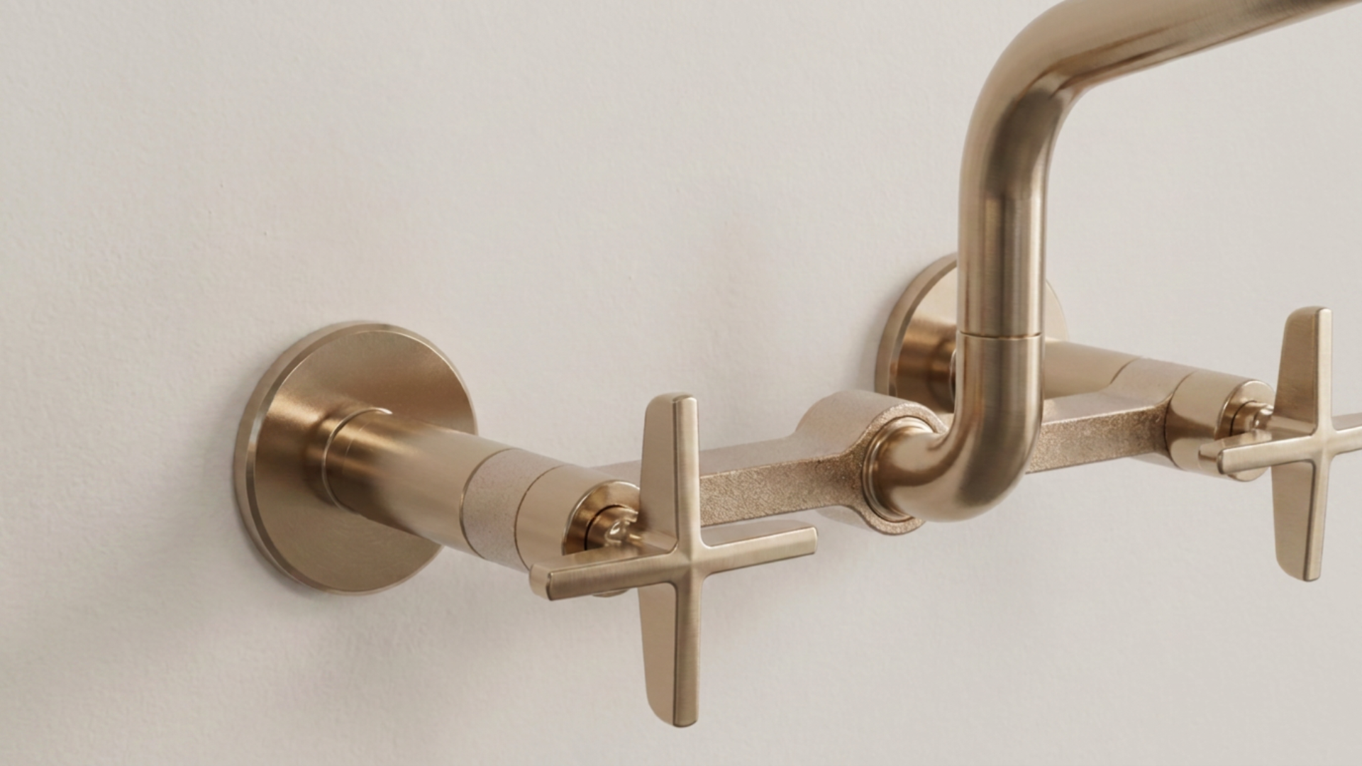 Brushed nickel plumbing pipe fixtures mounted on a white wall.