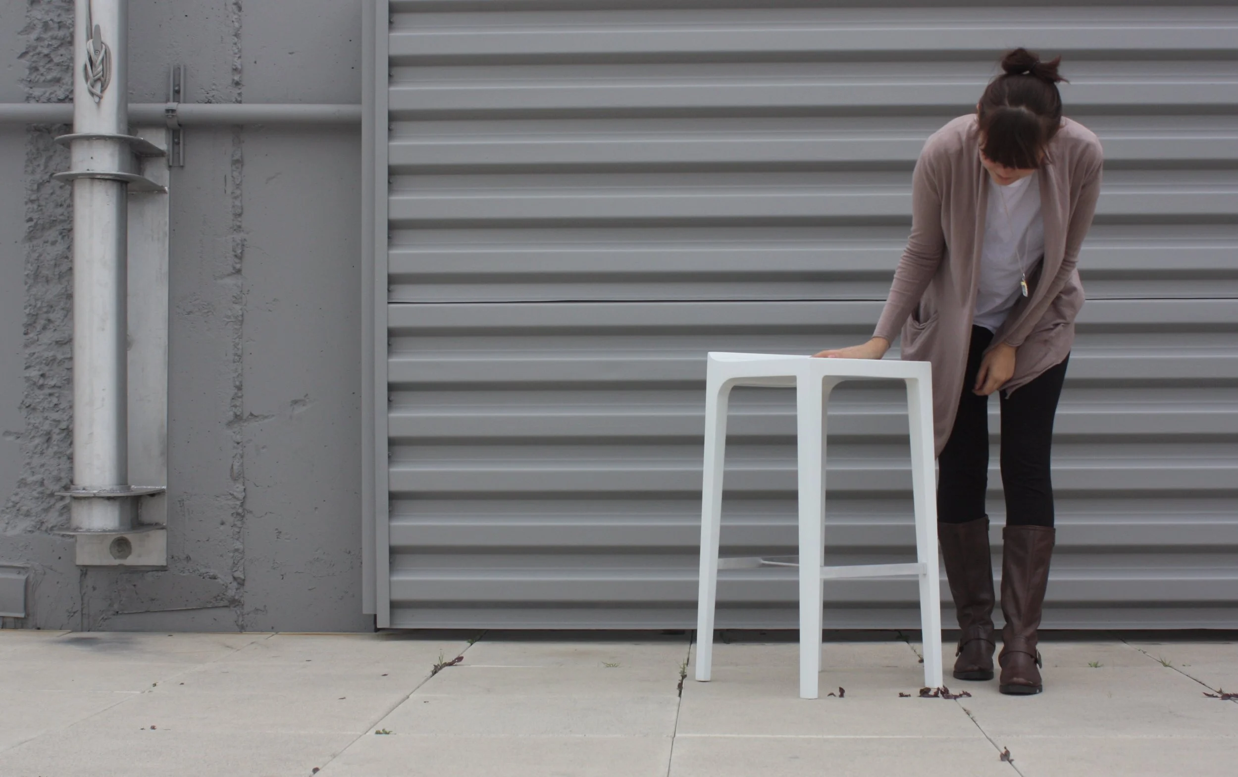 Woman in a cardigan standing beside a white table outdoors in front of a gray metal garage door