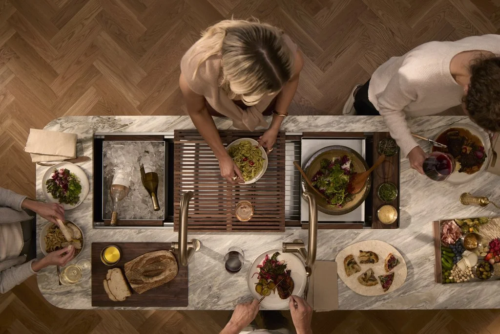 Overhead view of people preparing and serving a gourmet dinner around a marble kitchen island.