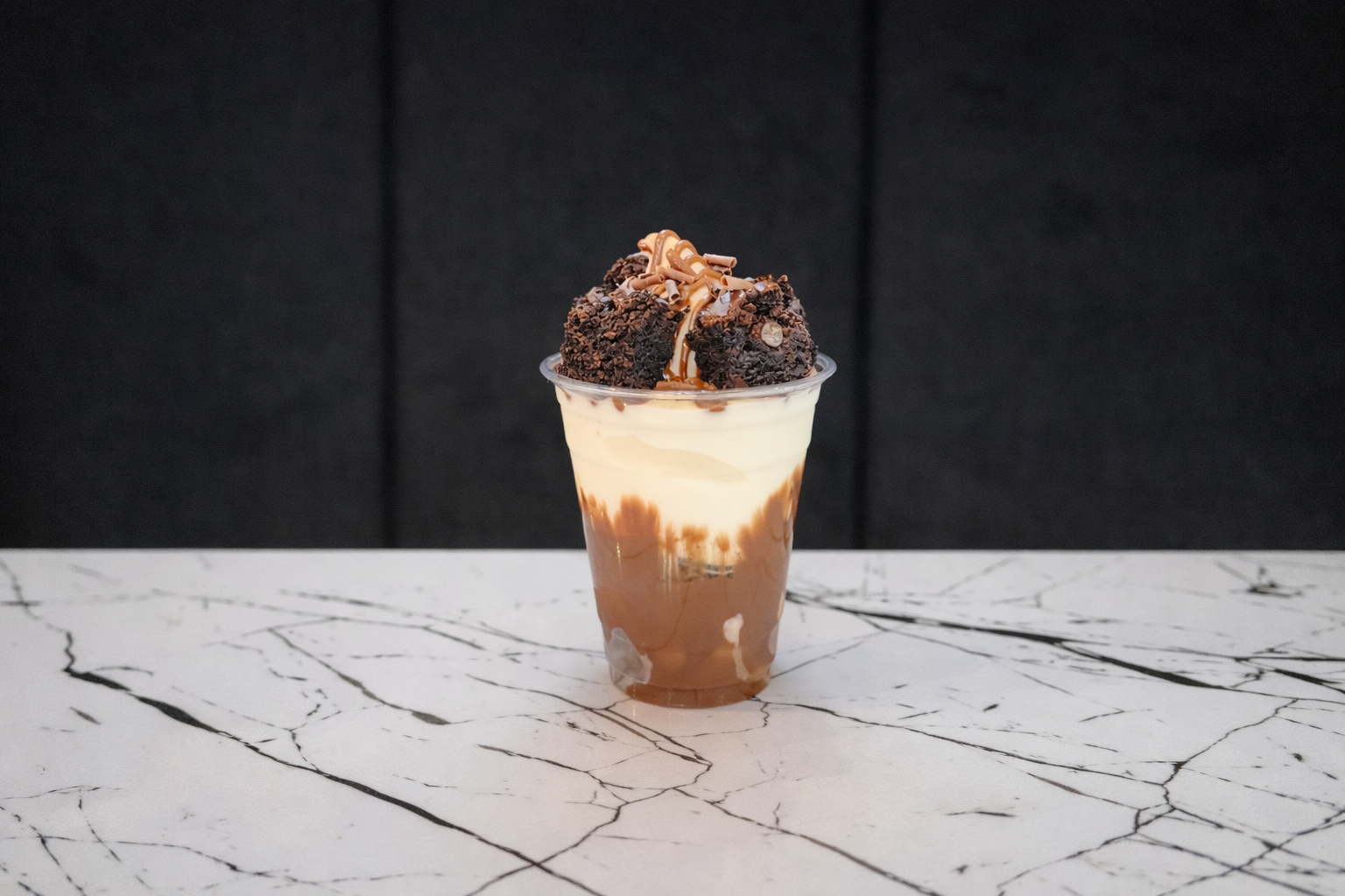 Chocolate Brownie sundae dessert with brownie and chocolate drizzle in a clear plastic cup on a white marble table.