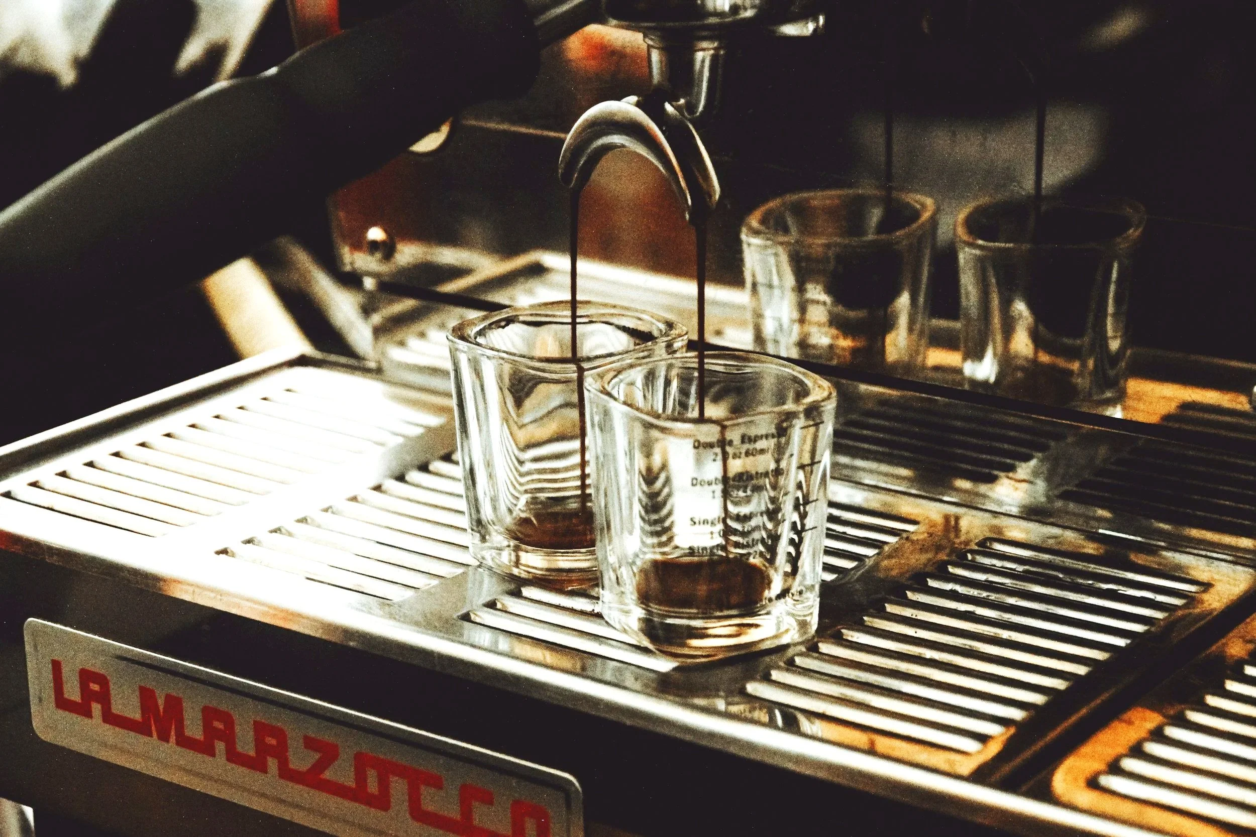 Espresso machine dispensing coffee into two glass cups on a commercial espresso machine.