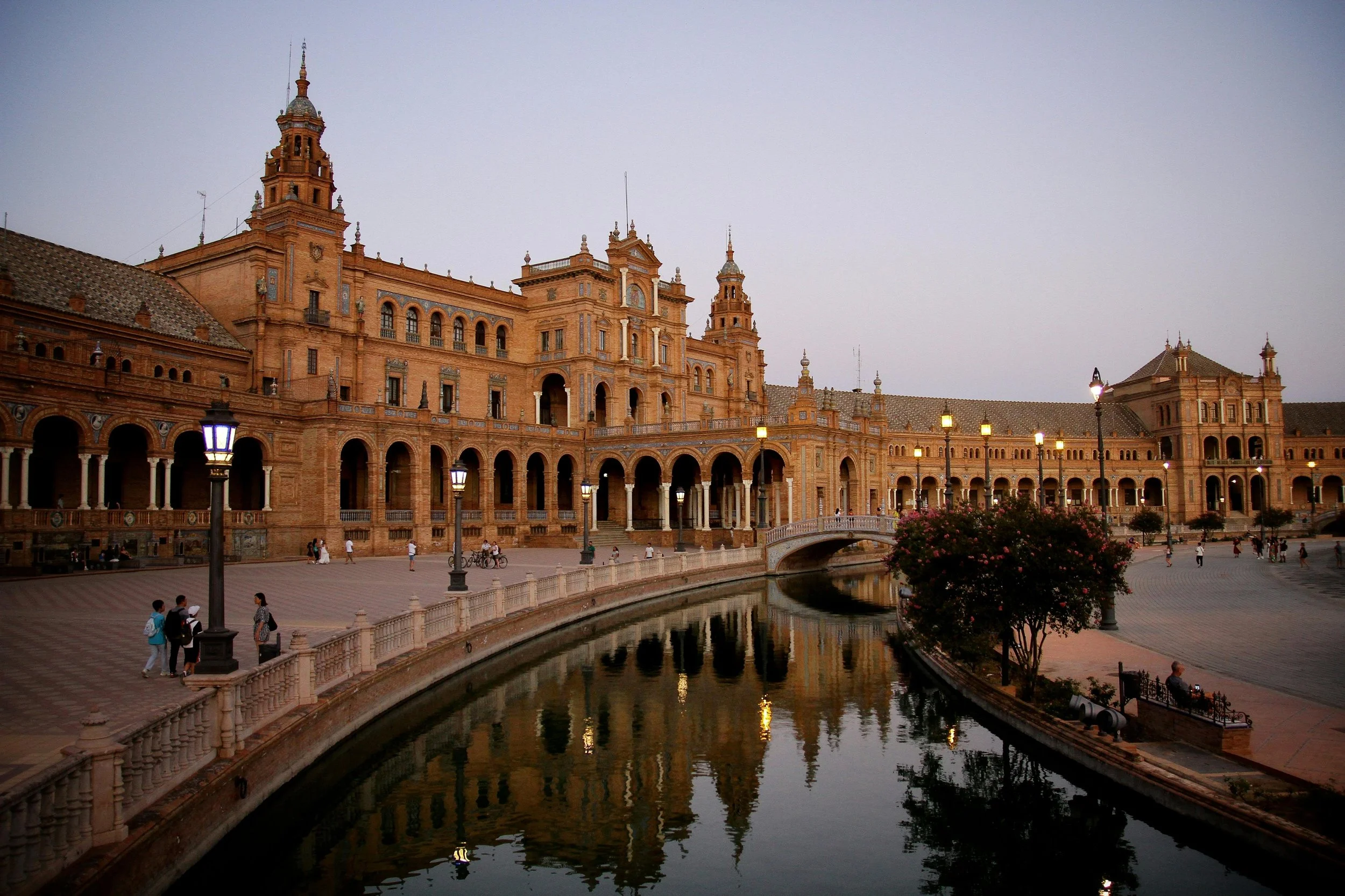 Plaza de España in Seville bathed in golden evening light, with ornate architecture reflecting in the canal below