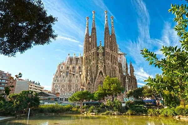 Sagrada Familia basilica in Barcelona with surrounding greenery and a partly cloudy sky