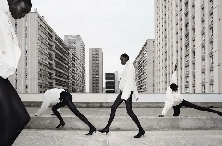 Fashion models in black and white outfits perform poses on a rooftop with a city skyline background.