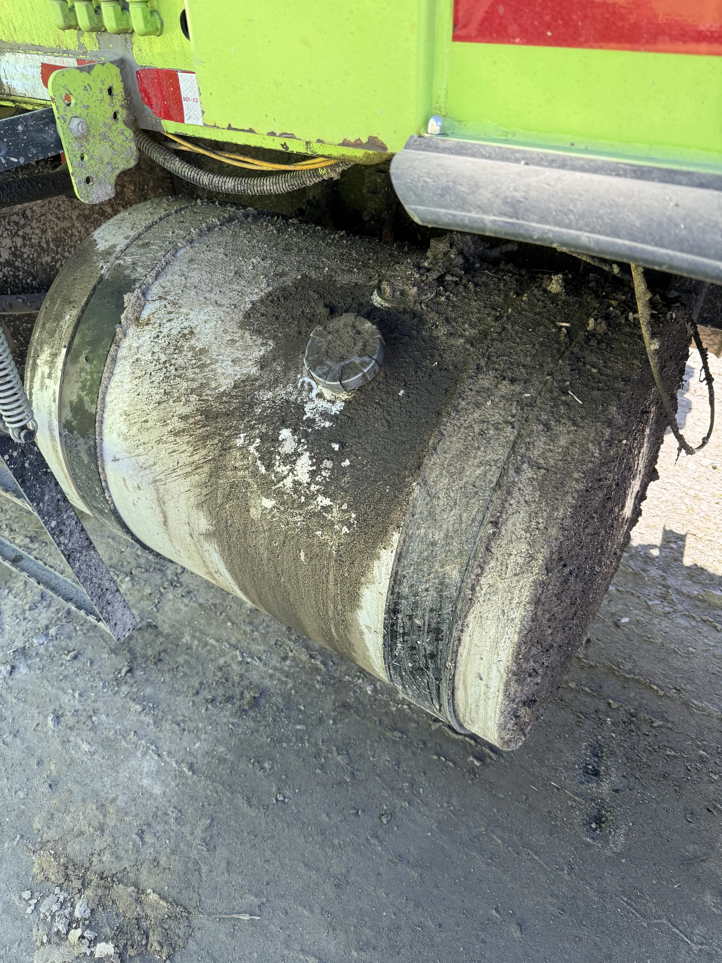 Close-up of a dirty, worn rubber wheel and metal assembly on construction equipment, on a gravel surface.