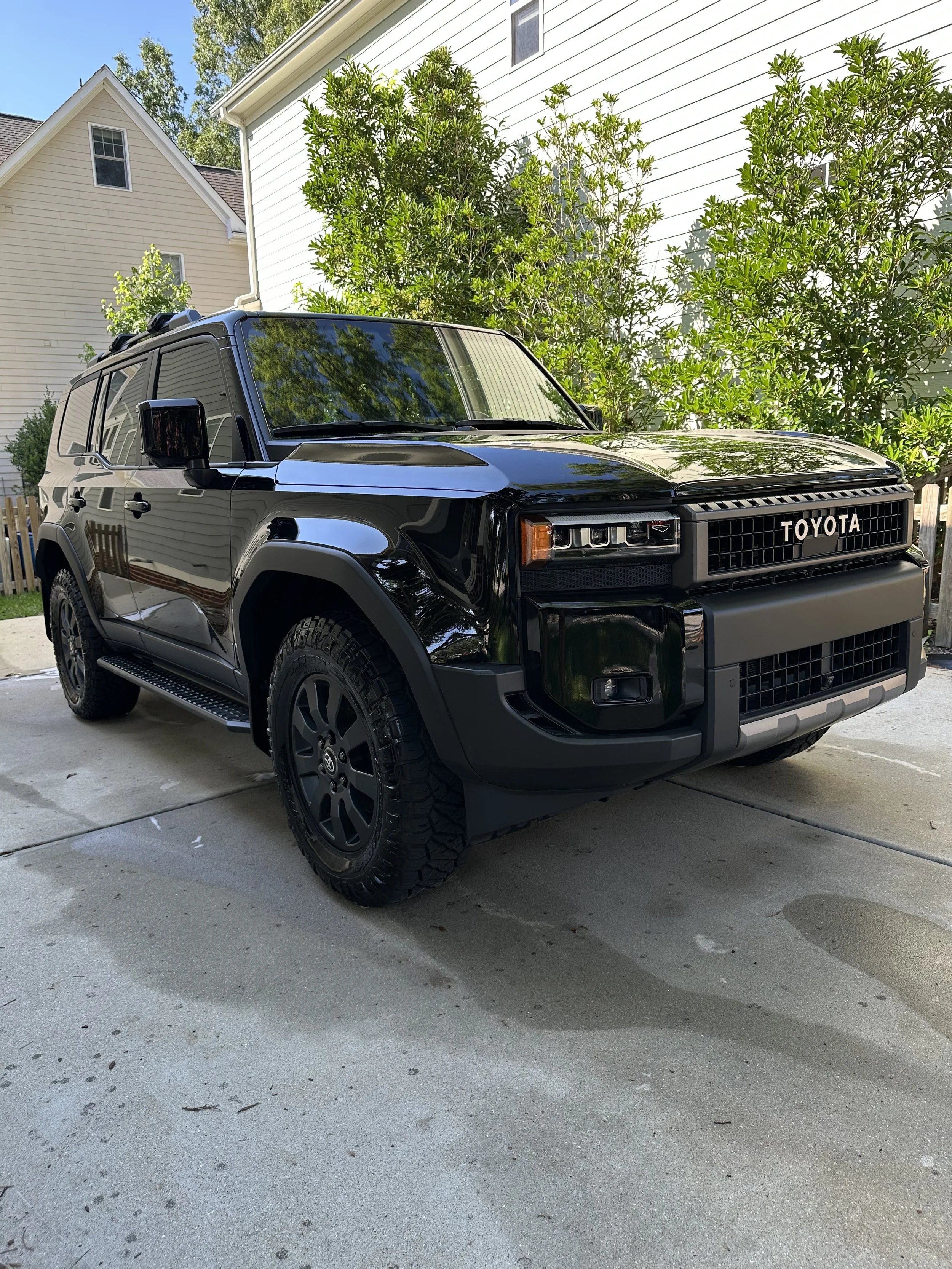 Black Toyota SUV parked on driveway in front of white house with green bushes
