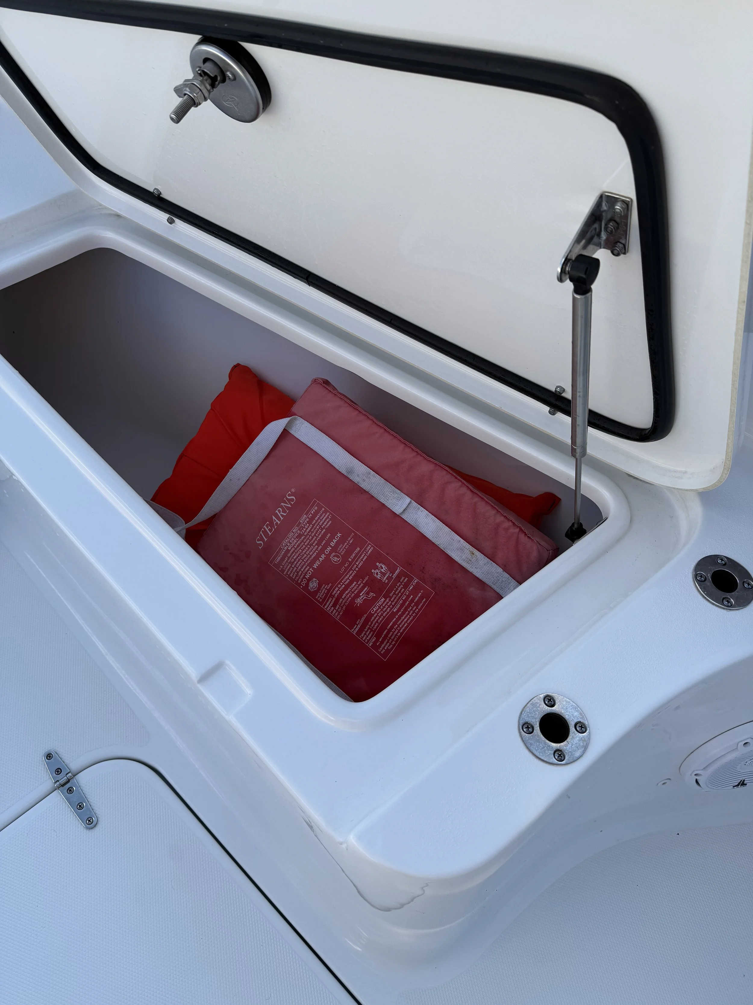 Open hatch of a boat with a red life jacket inside and hardware for securing the hatch.