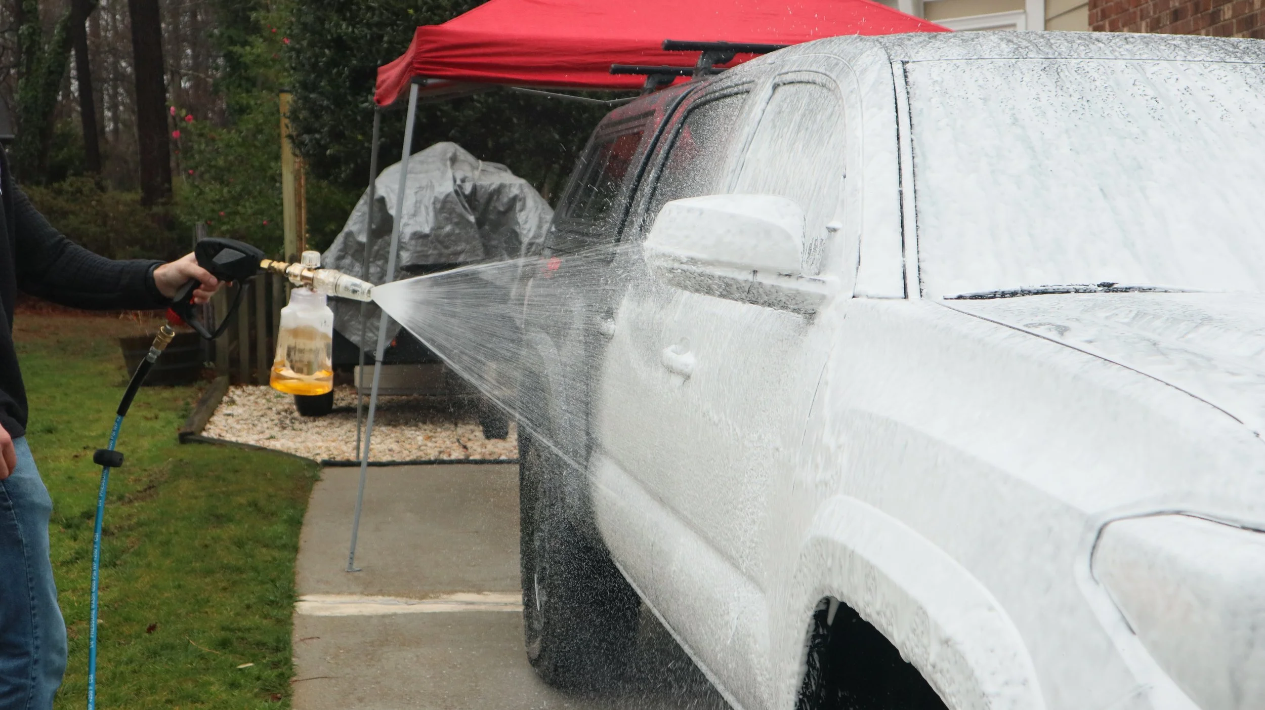 Person using a pressure washer to clean a white car outdoors.