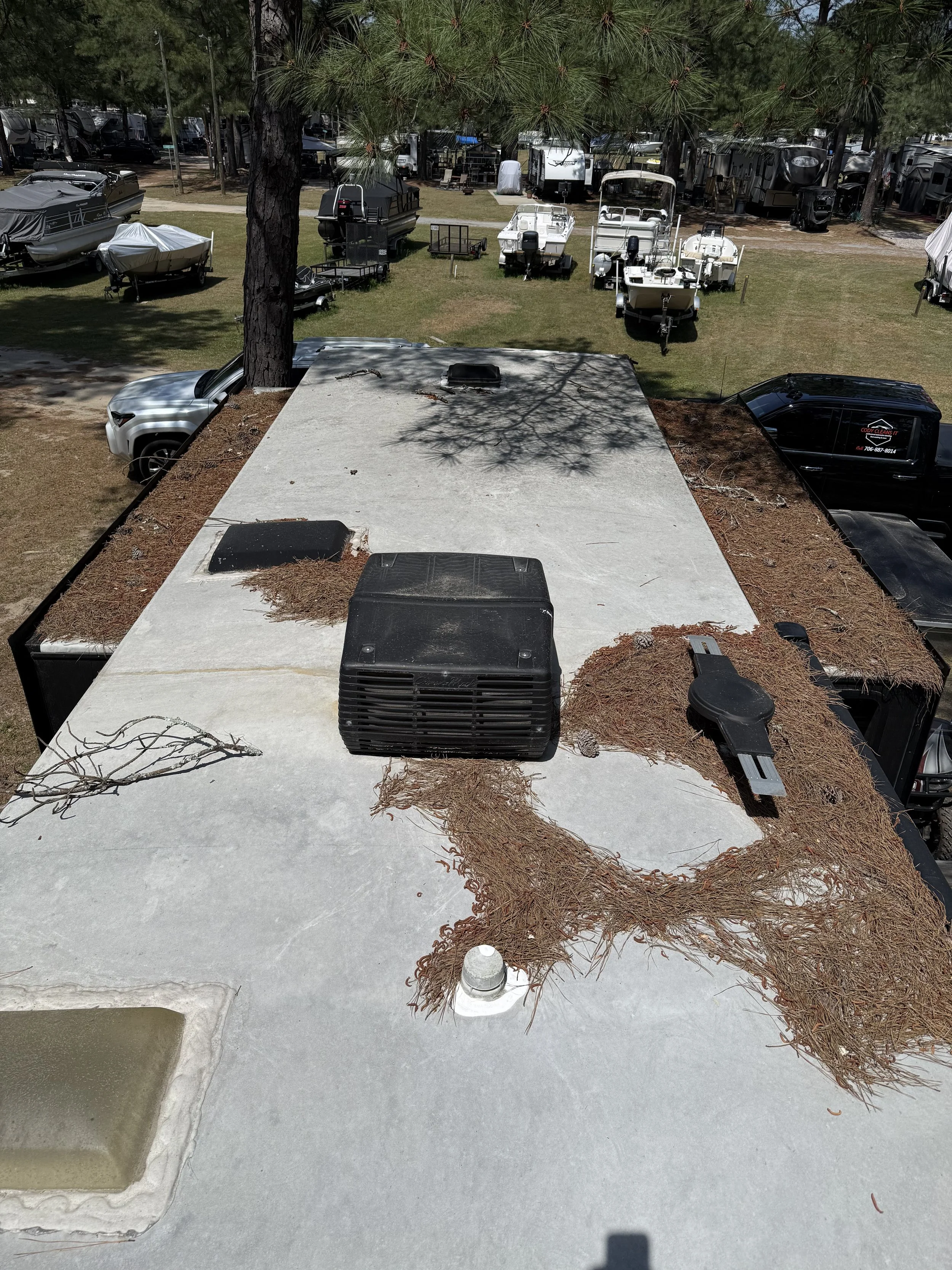 View from a rooftop showing a parking lot with boats, trailers, and cars, with trees casting shadows over the scene.