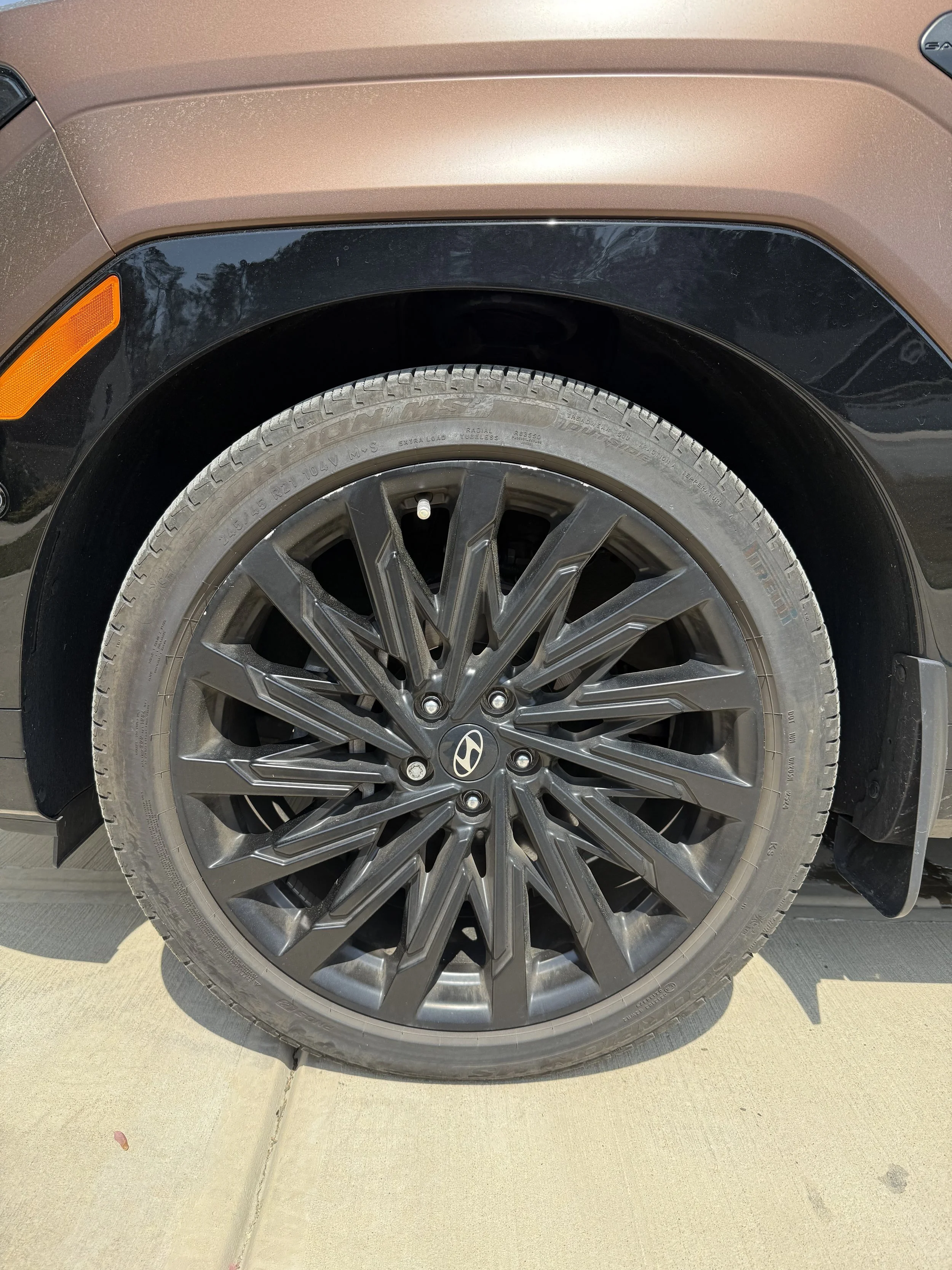 Close-up of a car wheel with a black alloy rim and the Hyundai logo, parked on a concrete driveway.