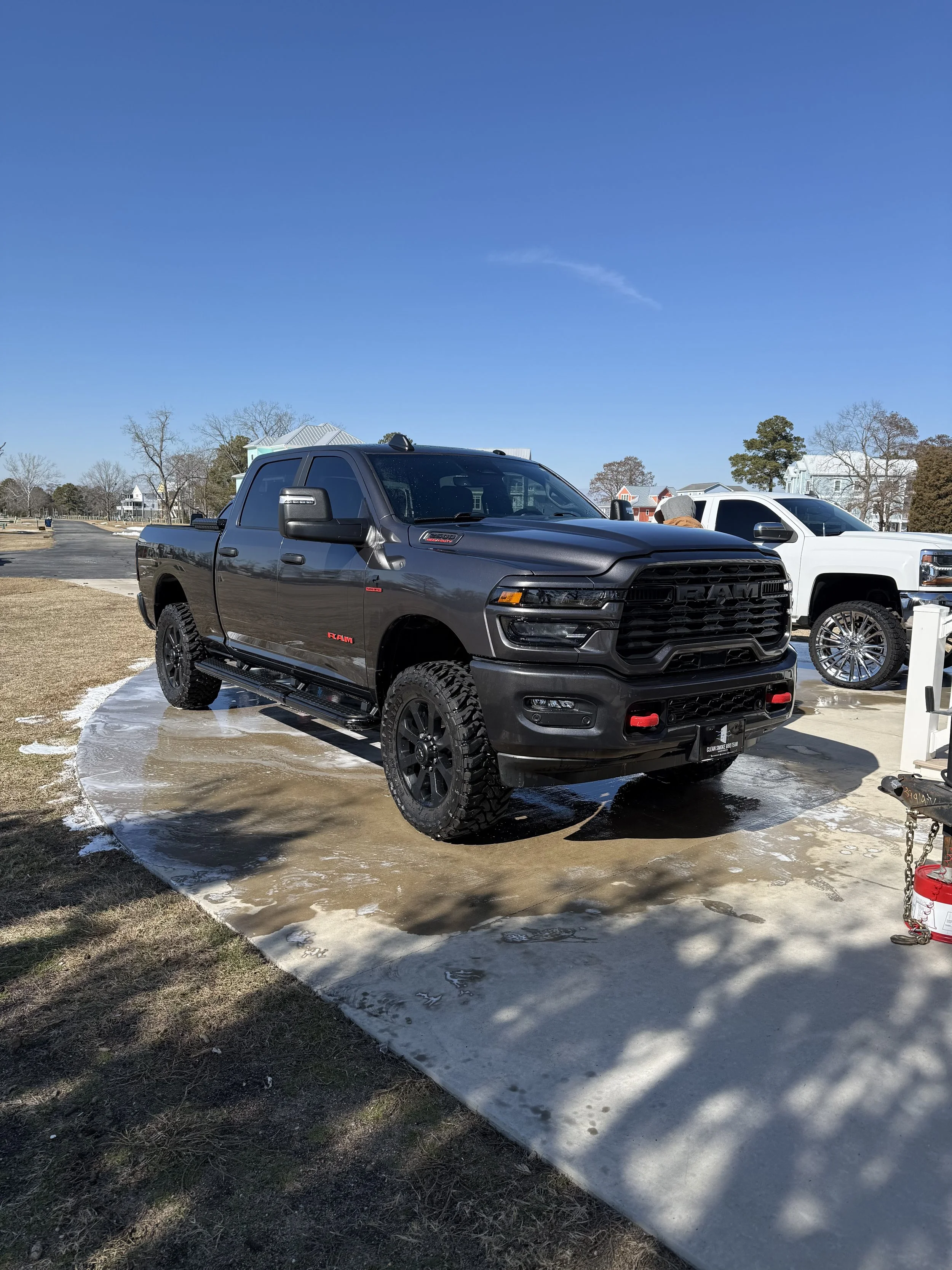 Black RAM pickup truck parked outside on a driveway with some soapy water and foam on the ground, with white trucks lined up behind it and houses in the background.