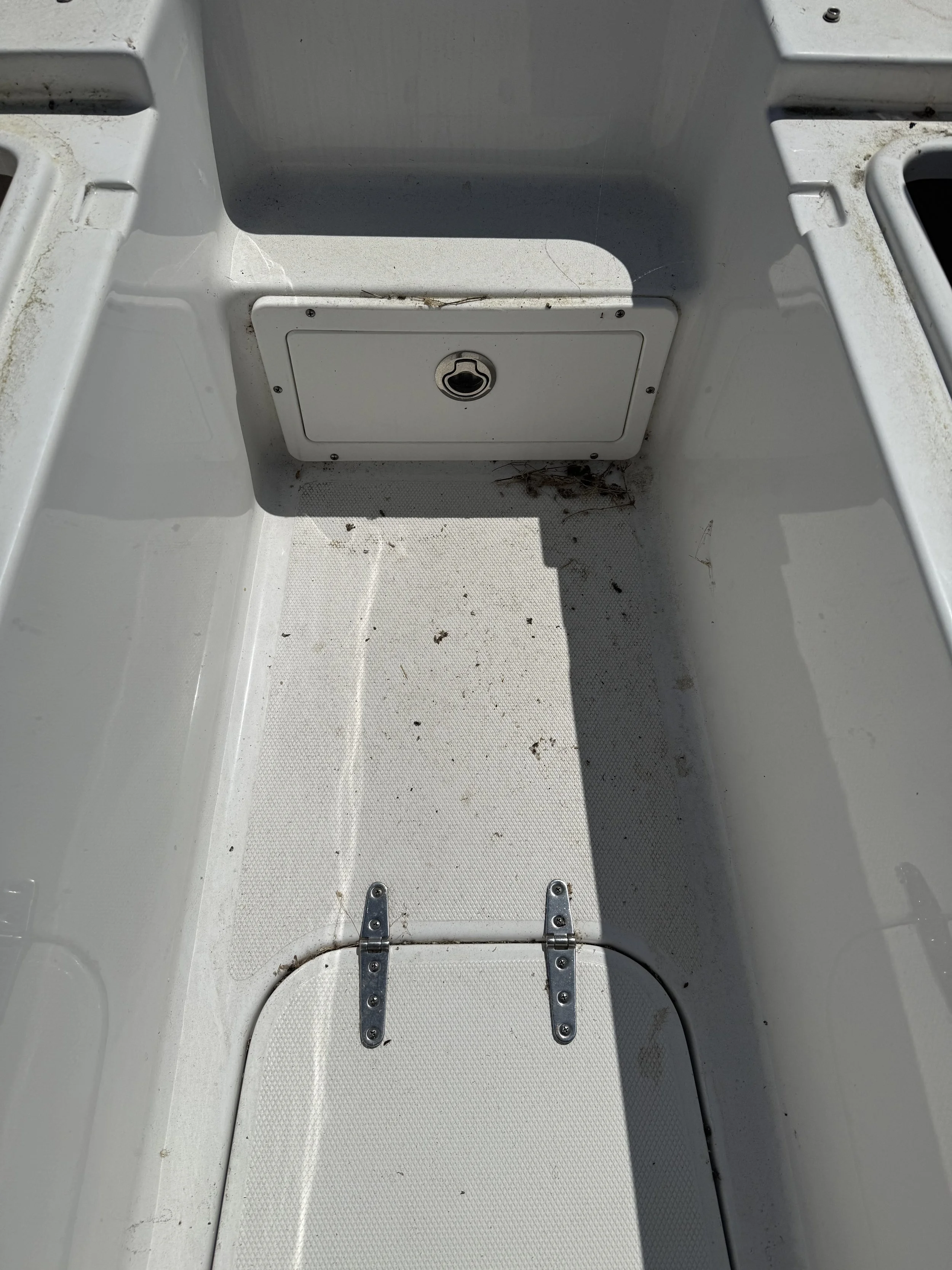 Empty boat interior with dirt and debris, metal hinges, and a small central hatch.