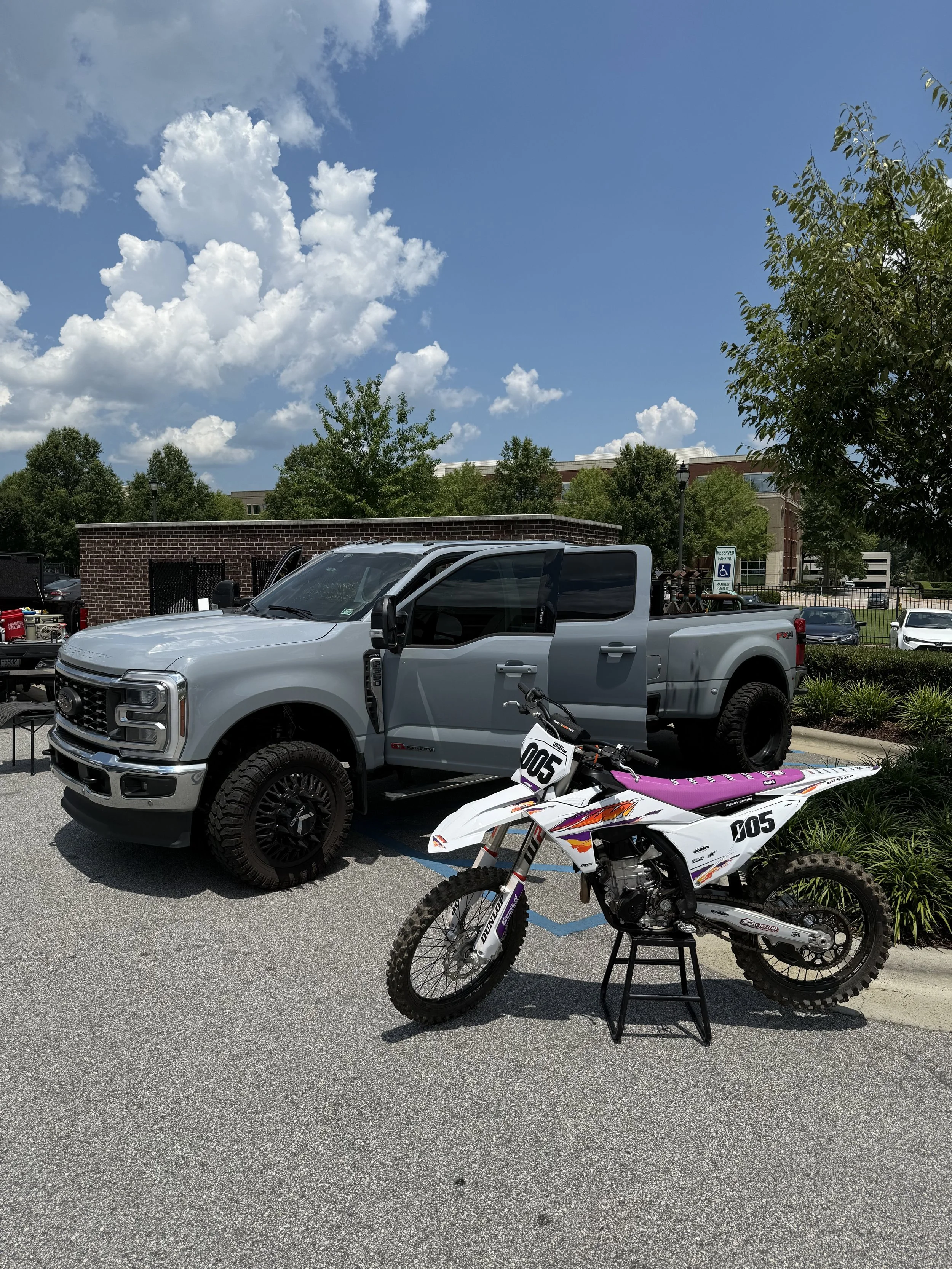 A white dirt bike with purple and orange accents on a black stand in a parking lot.