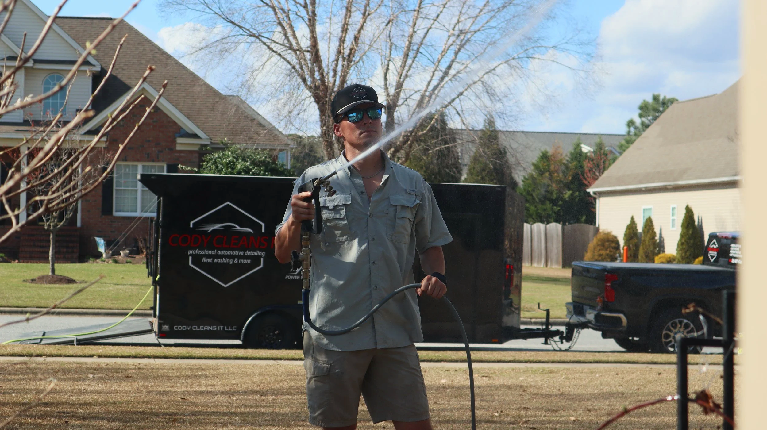 A man in sunglasses and a cap operating a pressure washer on a lawn.